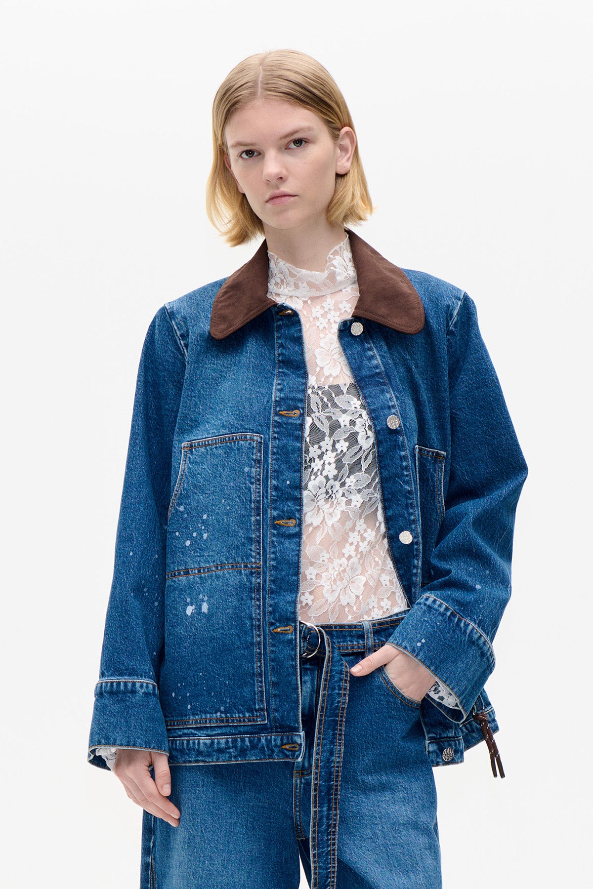 Front view of a model wearing a blue speckled denim jacket with an oversized brown collar over a white floral lace top.