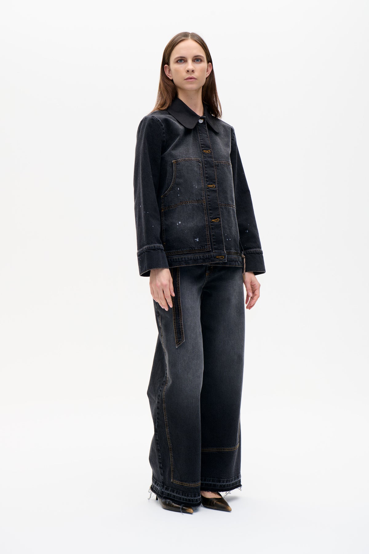 Front view of a model wearing a charcoal denim jacket with a large rounded collar, contrast stitching, patch pockets and light splatter details.