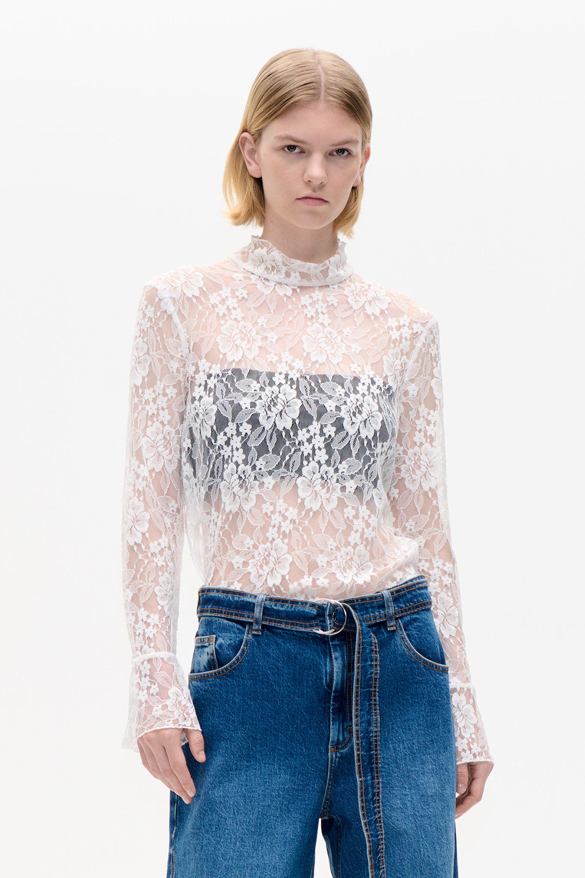 Front view of a sheer white floral lace top with a high neckline and long sleeves, styled with blue jeans.