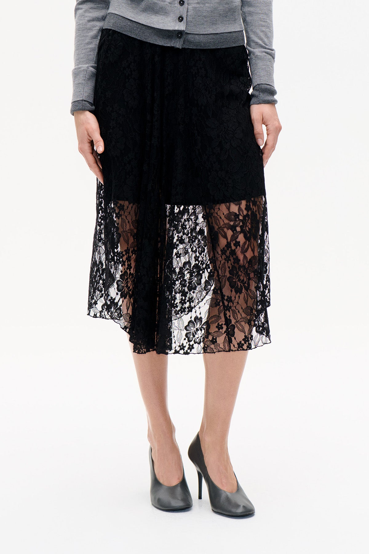 Front detail of a black floral lace midi skirt with a sheer lower panel, styled with a grey button-front cardigan.