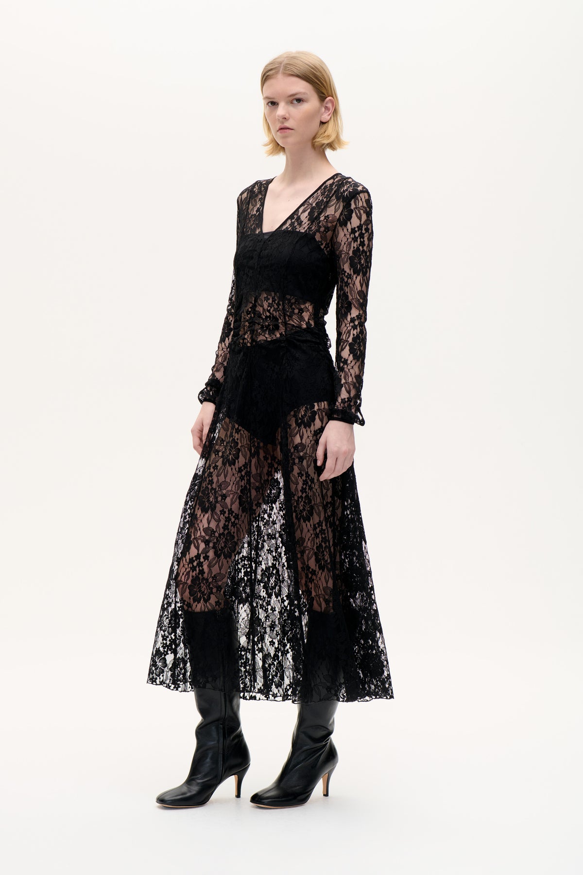 Front view of a model wearing a black floral lace dress with a V-neck, long sleeves and a sheer mid-length skirt.