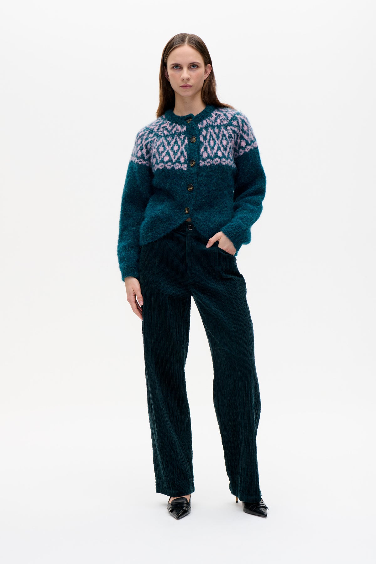Model wearing a teal button-front cardigan with a pink geometric yoke pattern and dark wide-leg corduroy trousers