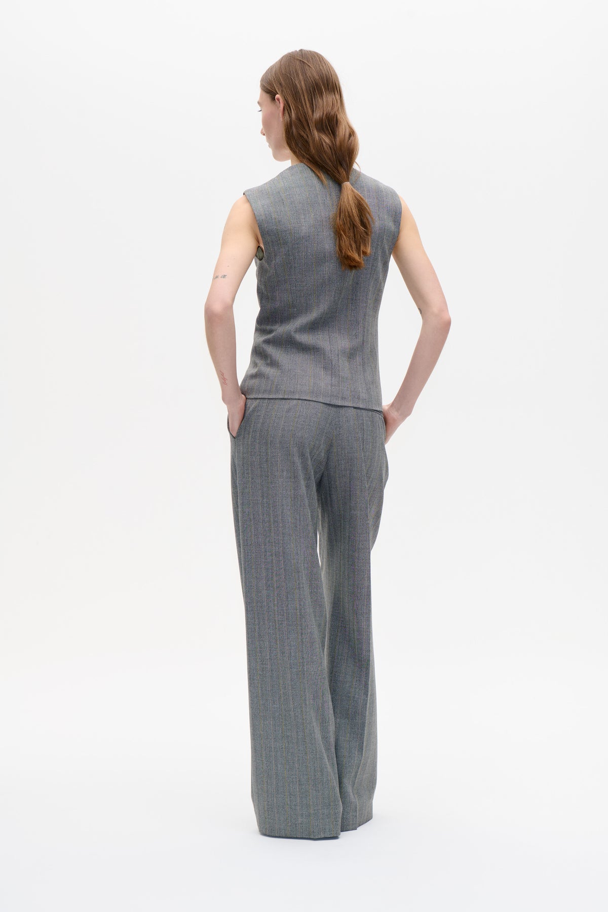 Back view of a model wearing a sleeveless grey tailored top and matching wide-leg trousers with fine vertical stripes.