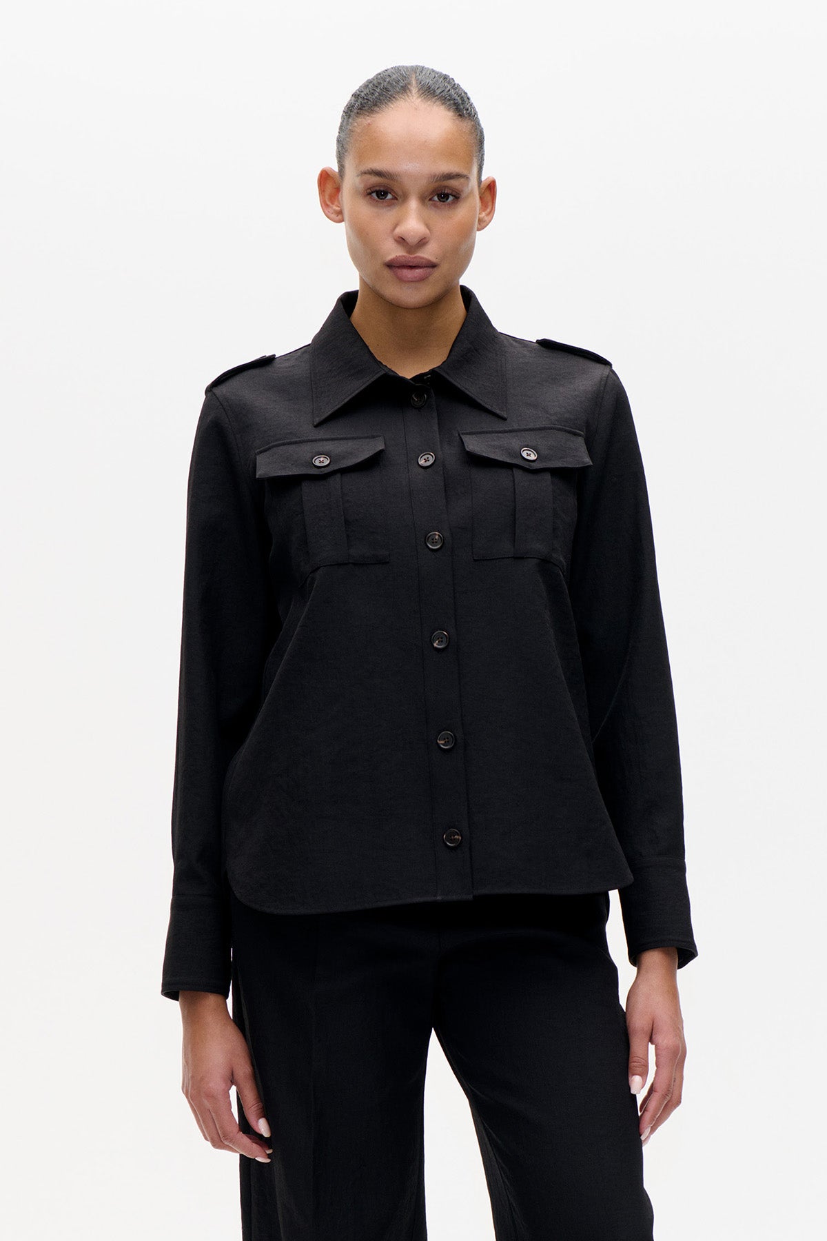 Front view of a model wearing a black long-sleeved button-up shirt with a pointed collar, shoulder tabs and flap chest pockets.