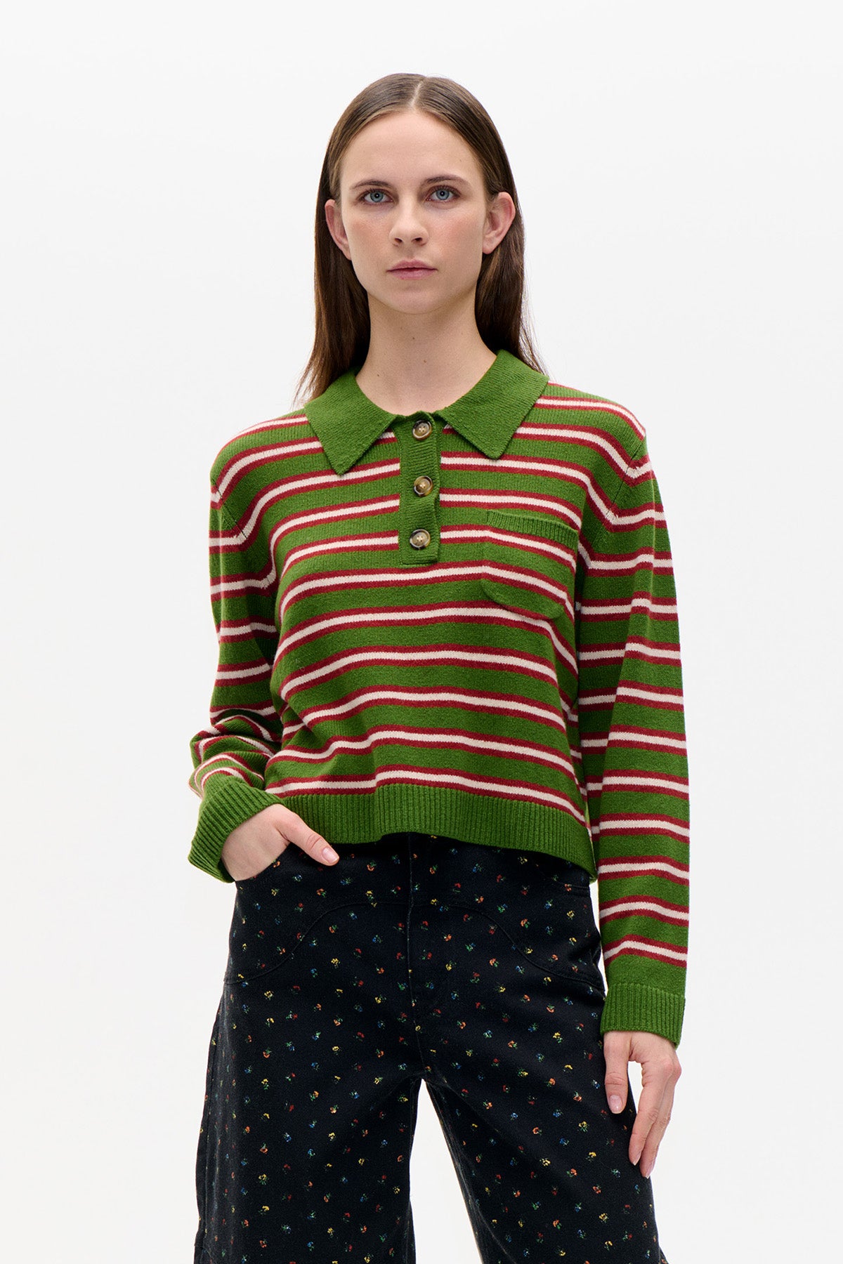 Front view of a green striped knit pullover with a pointed collar and button placket, styled with black floral-print trousers.