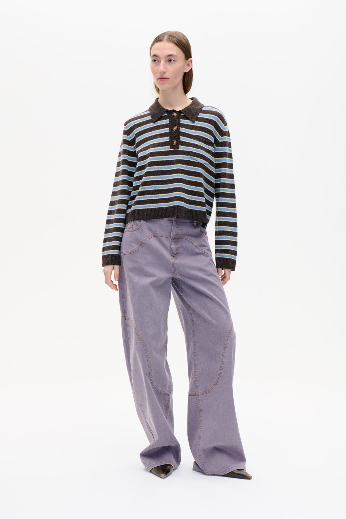 Model wearing a dark brown striped long-sleeve knit polo with a pointed collar and button placket, paired with lavender wide-leg trousers.