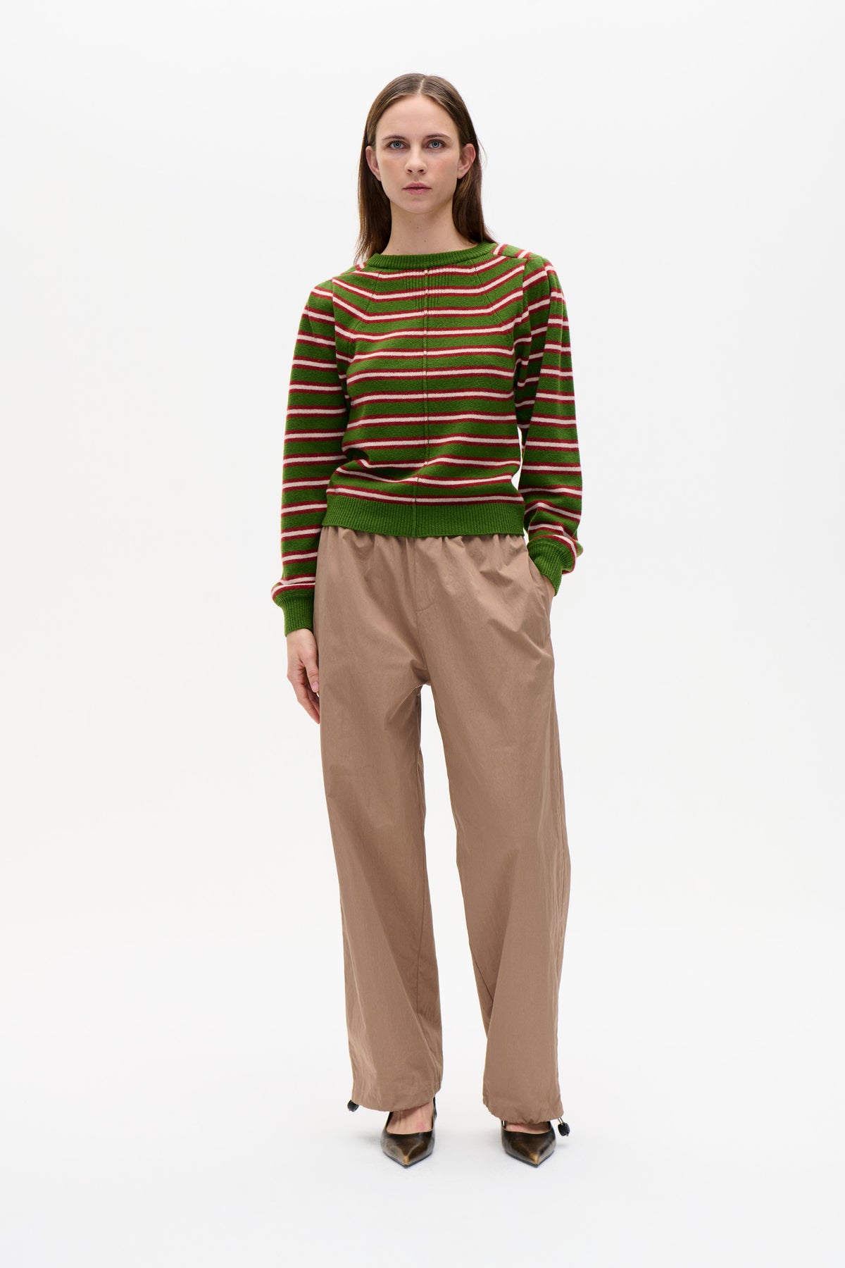 Model wearing a green crew-neck knit sweater with red and white horizontal stripes, paired with taupe wide-leg trousers.