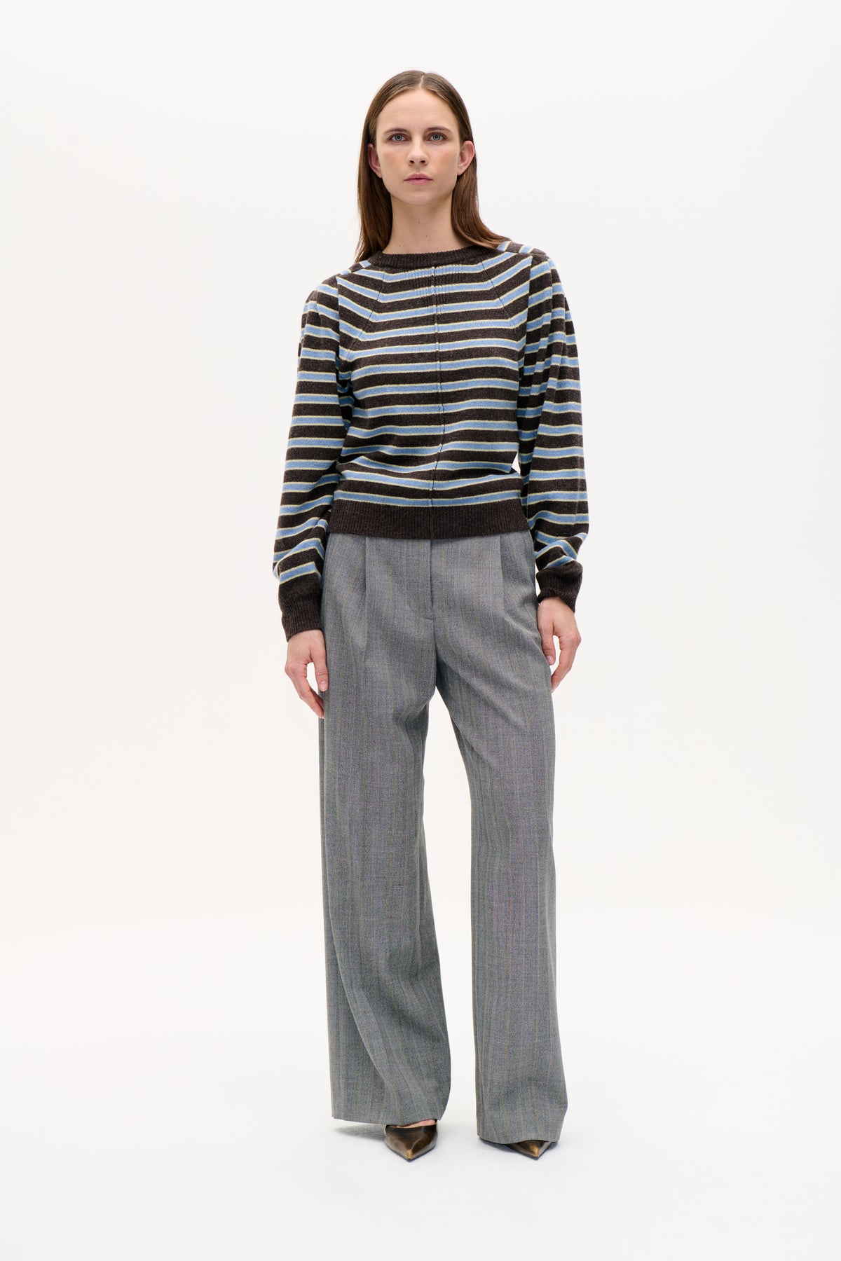 Front view of a model wearing a dark brown knit sweater with light blue and yellow horizontal stripes and grey pinstriped wide-leg trousers.