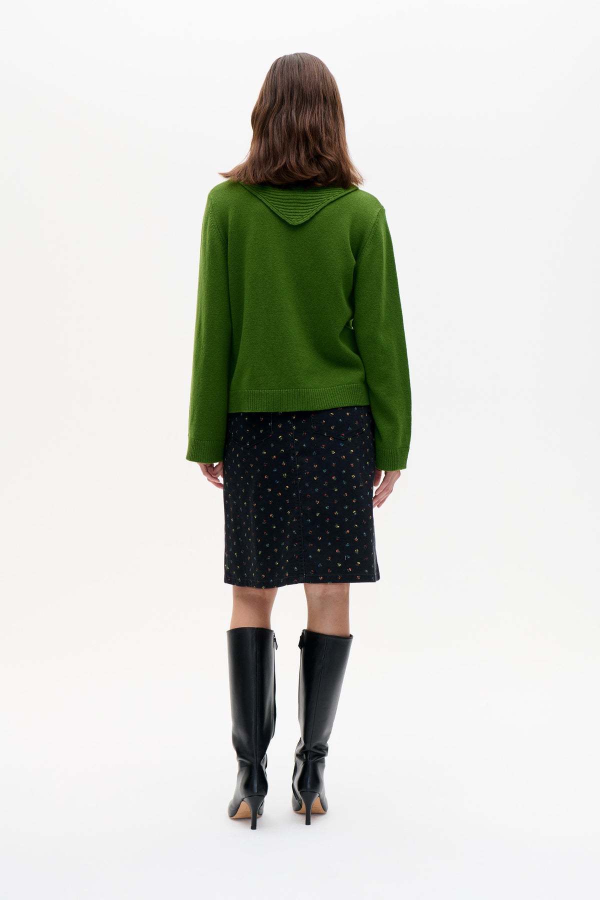 Back view of a model wearing a green knit hooded sweater and a black skirt with a tiny multicoloured floral print.