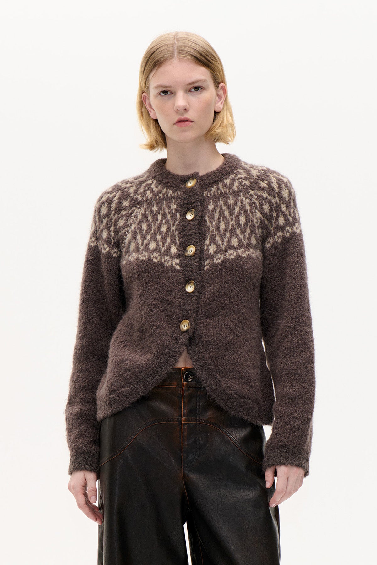 Front view of a dark brown knitted cardigan with cream patterned shoulders, button fastening and round neckline, paired with black trousers.