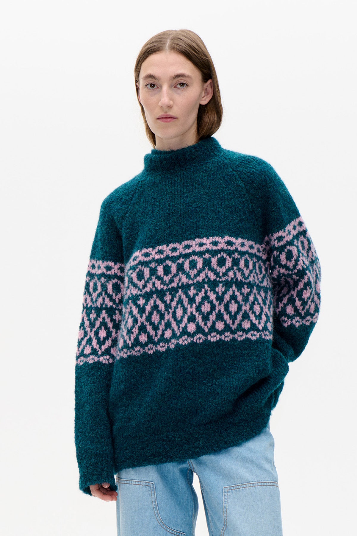 Front view of a teal high-neck knitted sweater with a pink geometric pattern across the chest and sleeves.