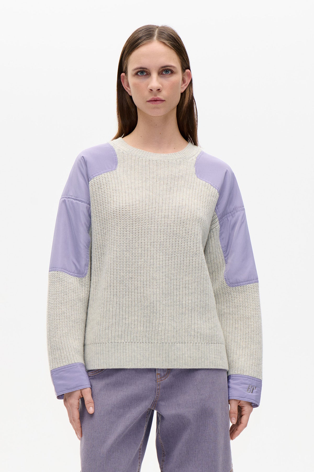 Front view of a cream chunky-knit sweater with lavender fabric panels at the shoulders, sleeves and cuffs, worn with lavender jeans.