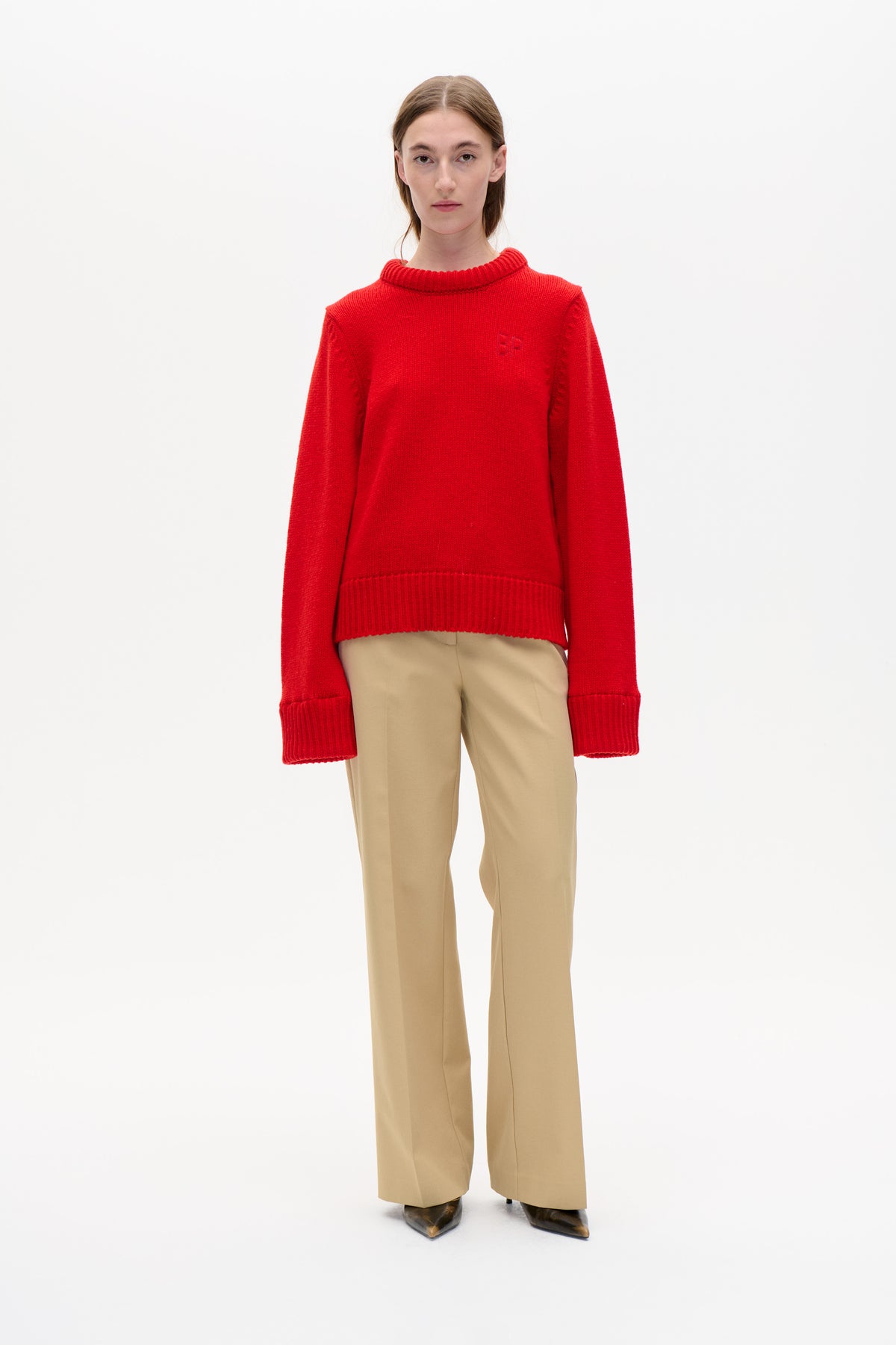 Front view of a model wearing a bright red ribbed-knit sweater with a high crew neckline and beige wide-leg trousers.