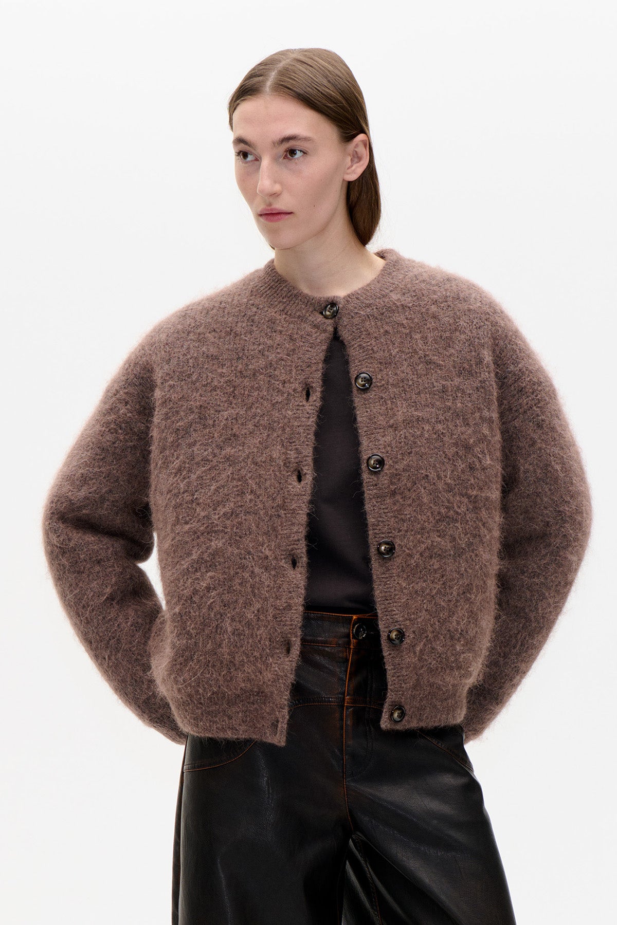 Front view of a fuzzy taupe-brown button-front cardigan with a round neckline and voluminous sleeves, worn with black trousers.
