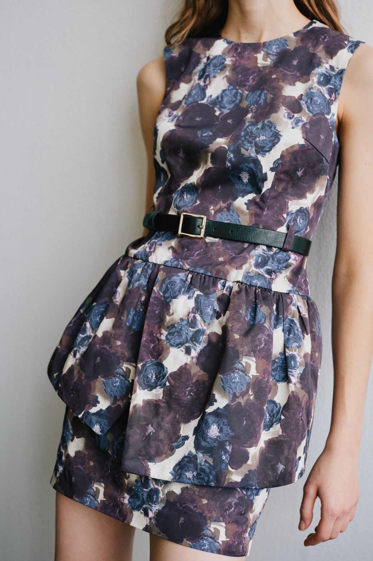 Gros plan d'une robe couleur crème à grand imprimé floral violet et bleu, taille froncée et ceinture vert foncé à boucle dorée.