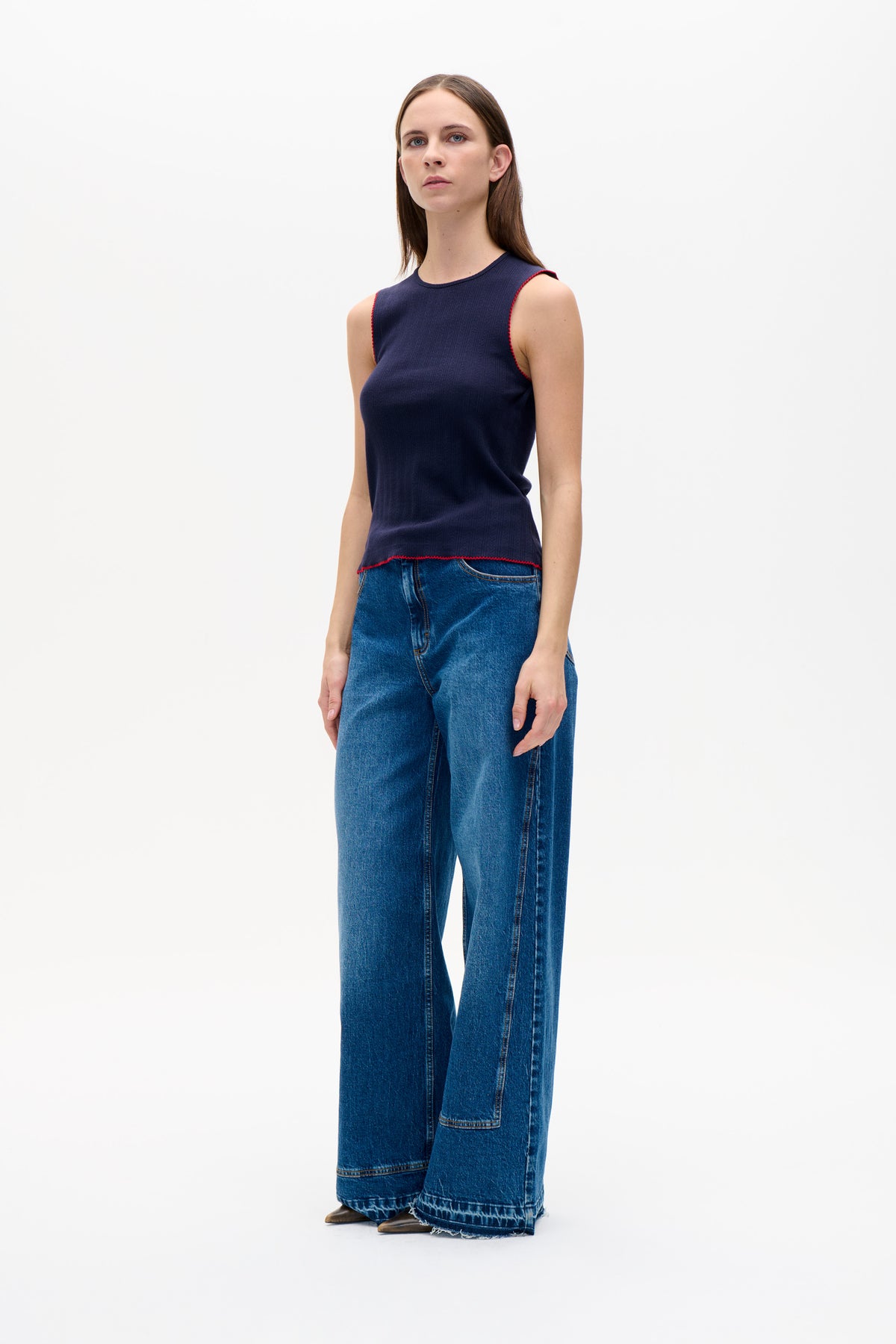 Front view of a model wearing a navy sleeveless top with subtle vertical texture and red trim, paired with wide-leg blue jeans.