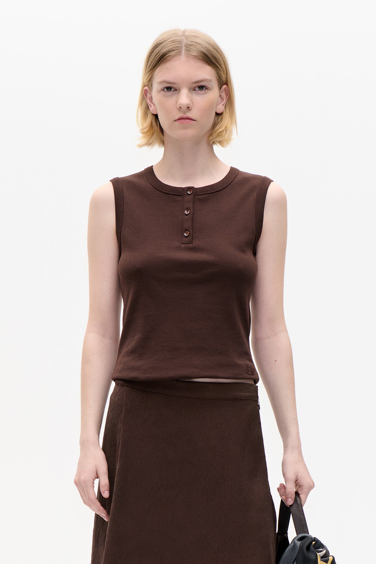 Front view of a dark brown sleeveless top with a round neckline and three-button placket, paired with a tonal textured skirt.