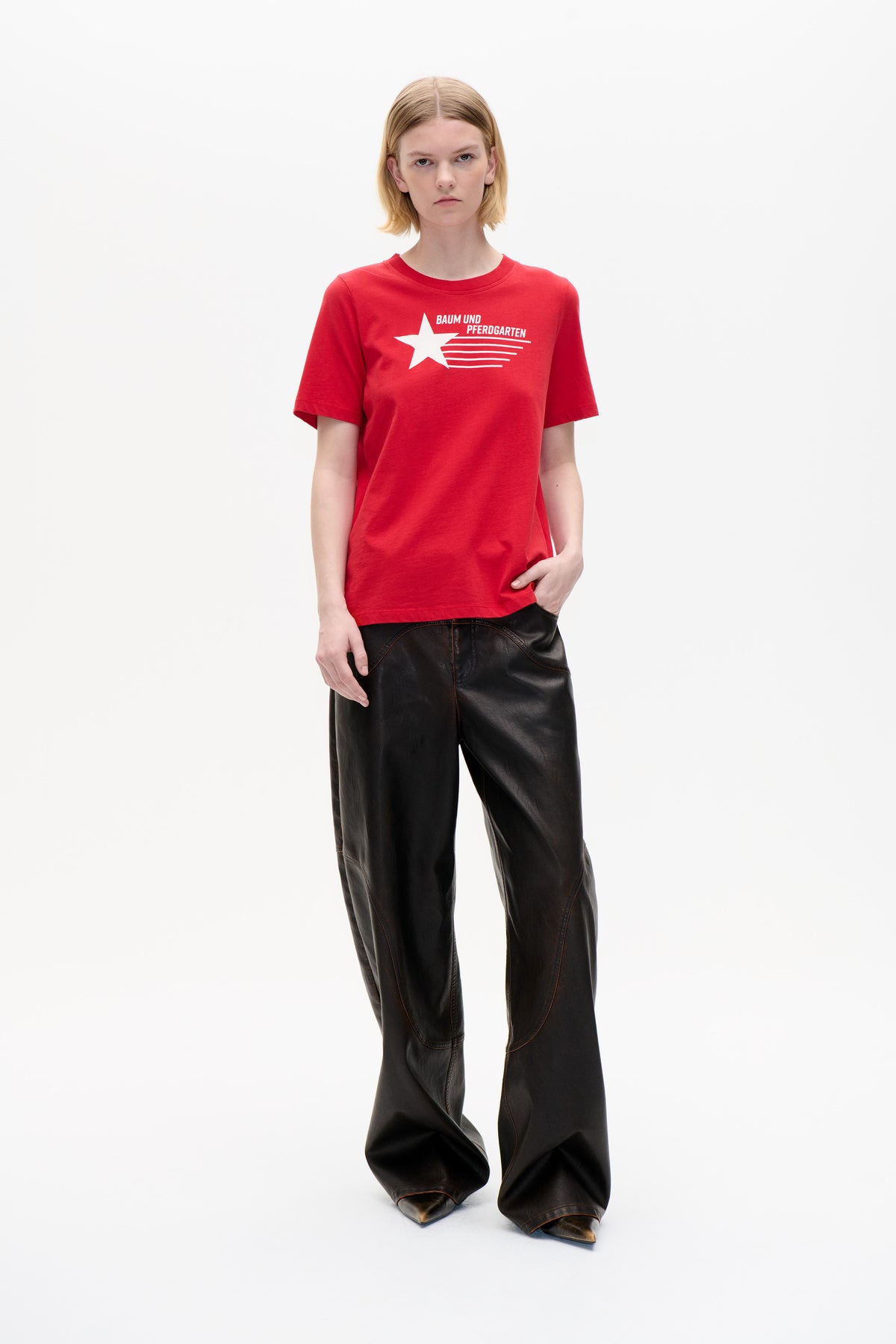 Model wearing a red short-sleeved T-shirt with a white Baum und Pferdgarten star graphic and black wide-leg trousers.