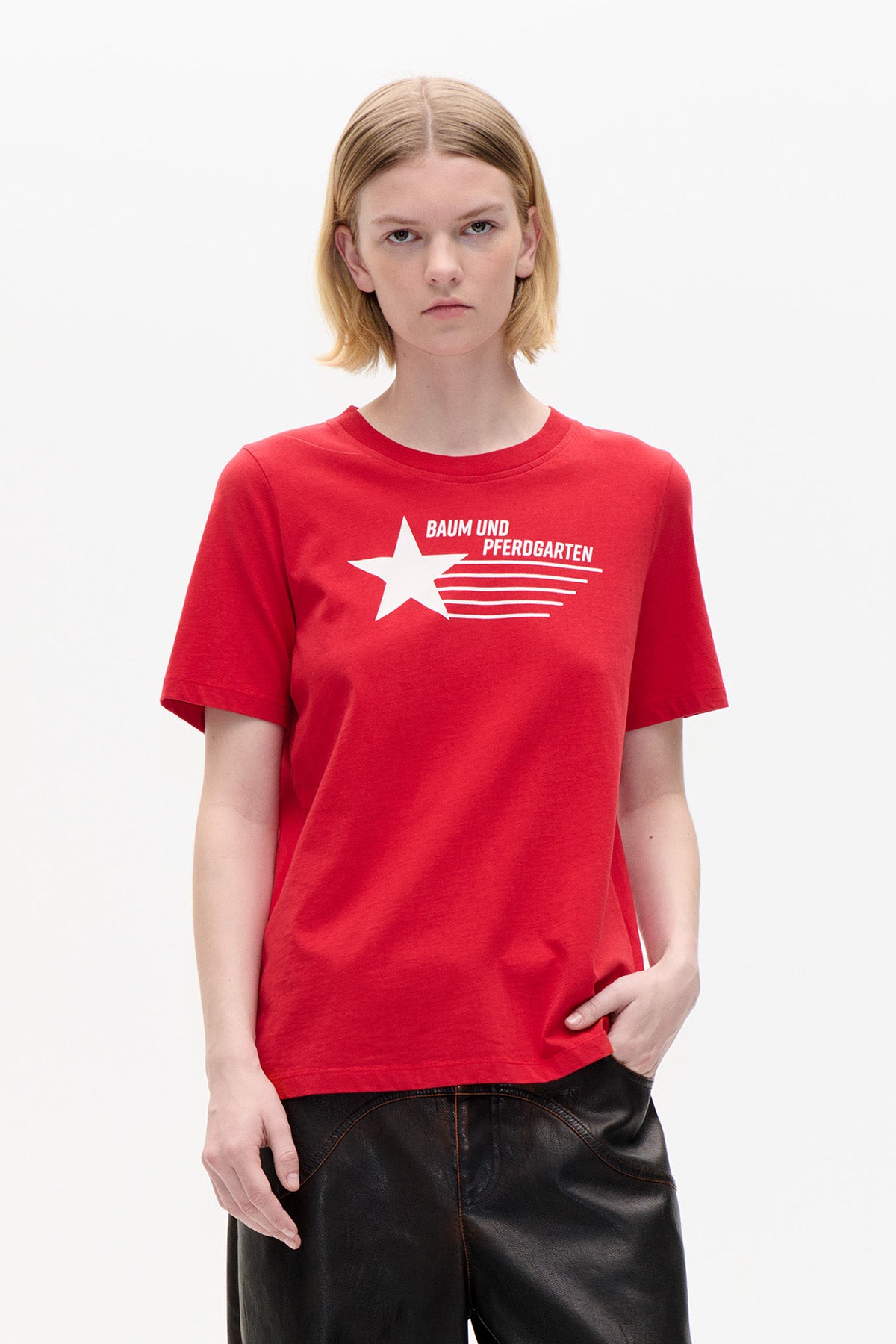 Model wearing a red crew-neck T-shirt with a white Baum und Pferdgarten star logo and text on the front.
