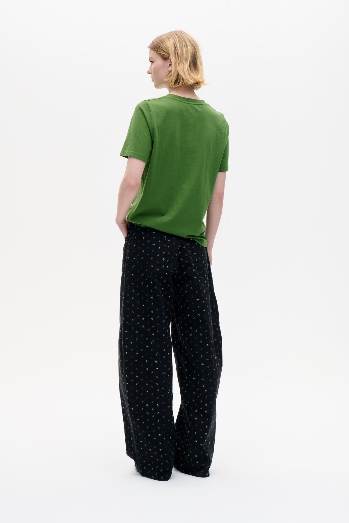 Model shown from the back wearing a plain green short-sleeved T-shirt and black wide-leg trousers with tiny multicoloured floral print.
