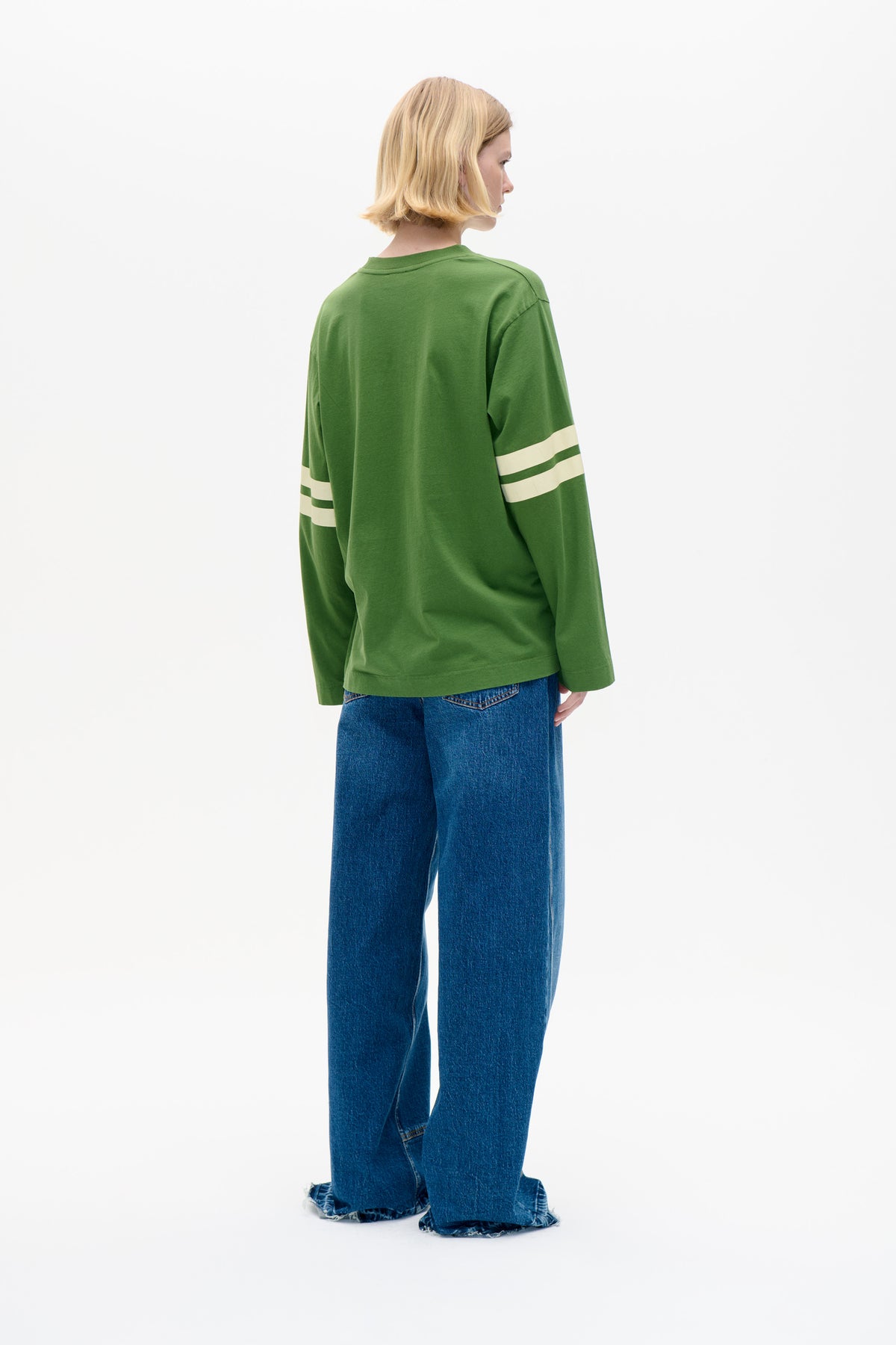 Back view of a model wearing a green long-sleeved top with cream sleeve stripes and wide-leg blue jeans.