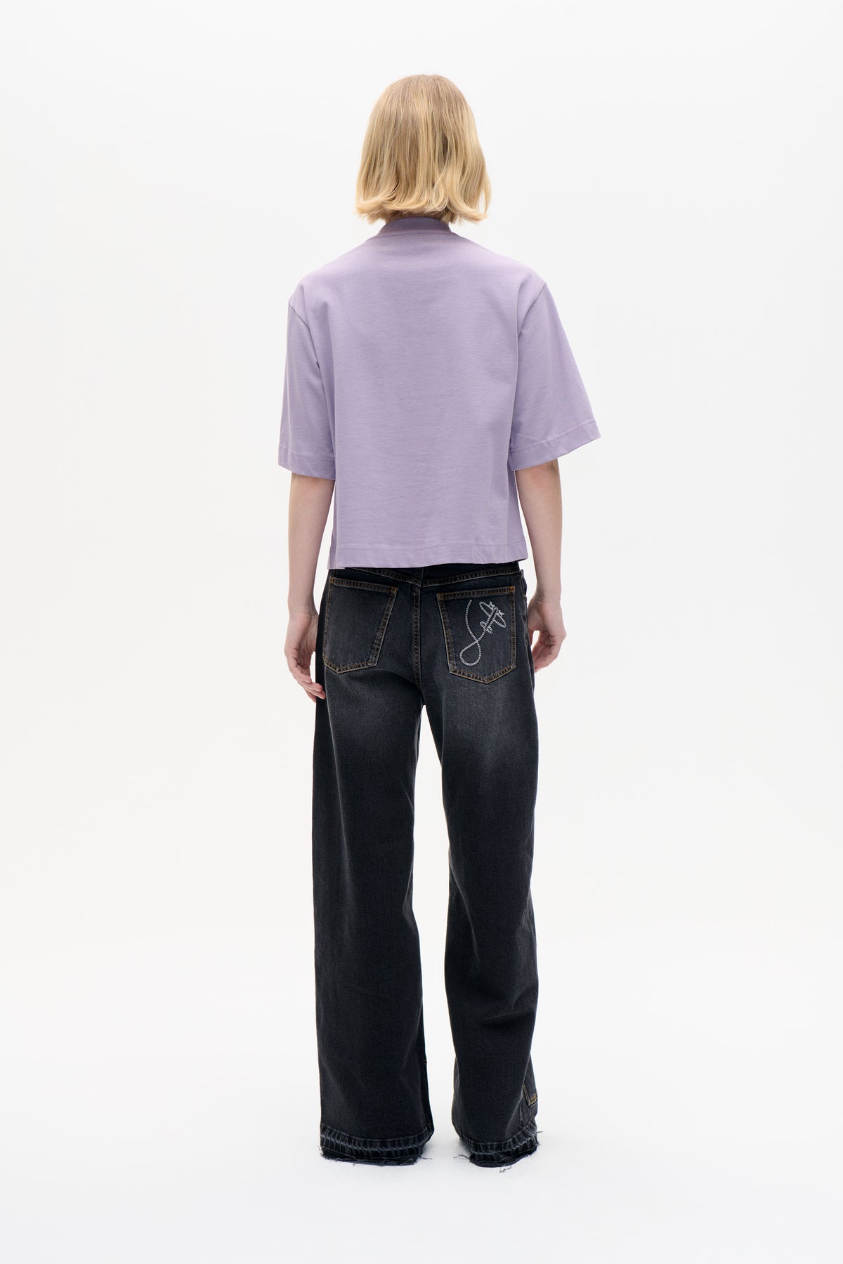 Back view of a model in a plain lilac short-sleeve T-shirt and charcoal wide-leg jeans with embroidered back-pocket detail.