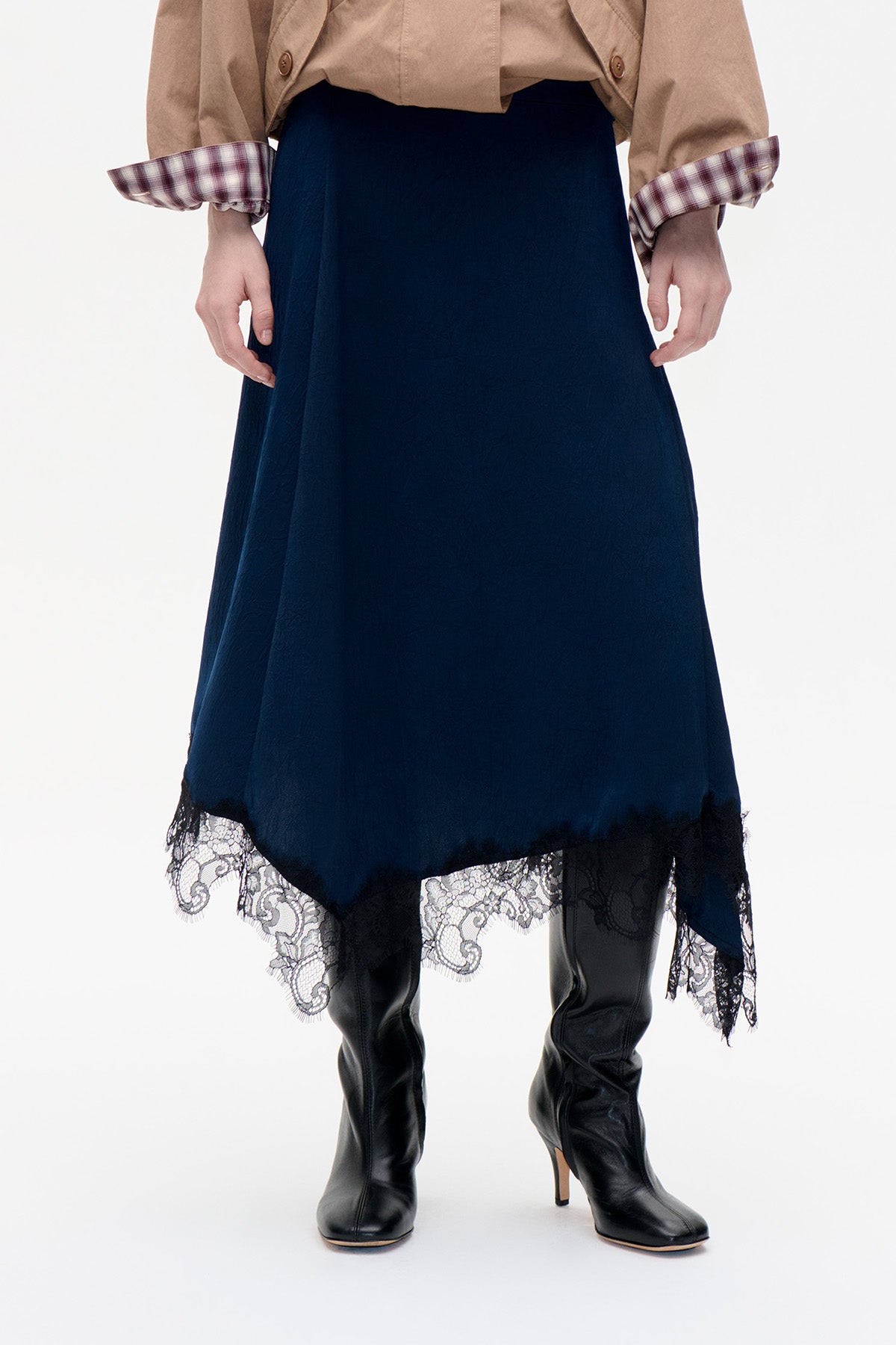 Front detail of a dark navy skirt with an asymmetric hem and black lace edging, styled with black knee-high boots.