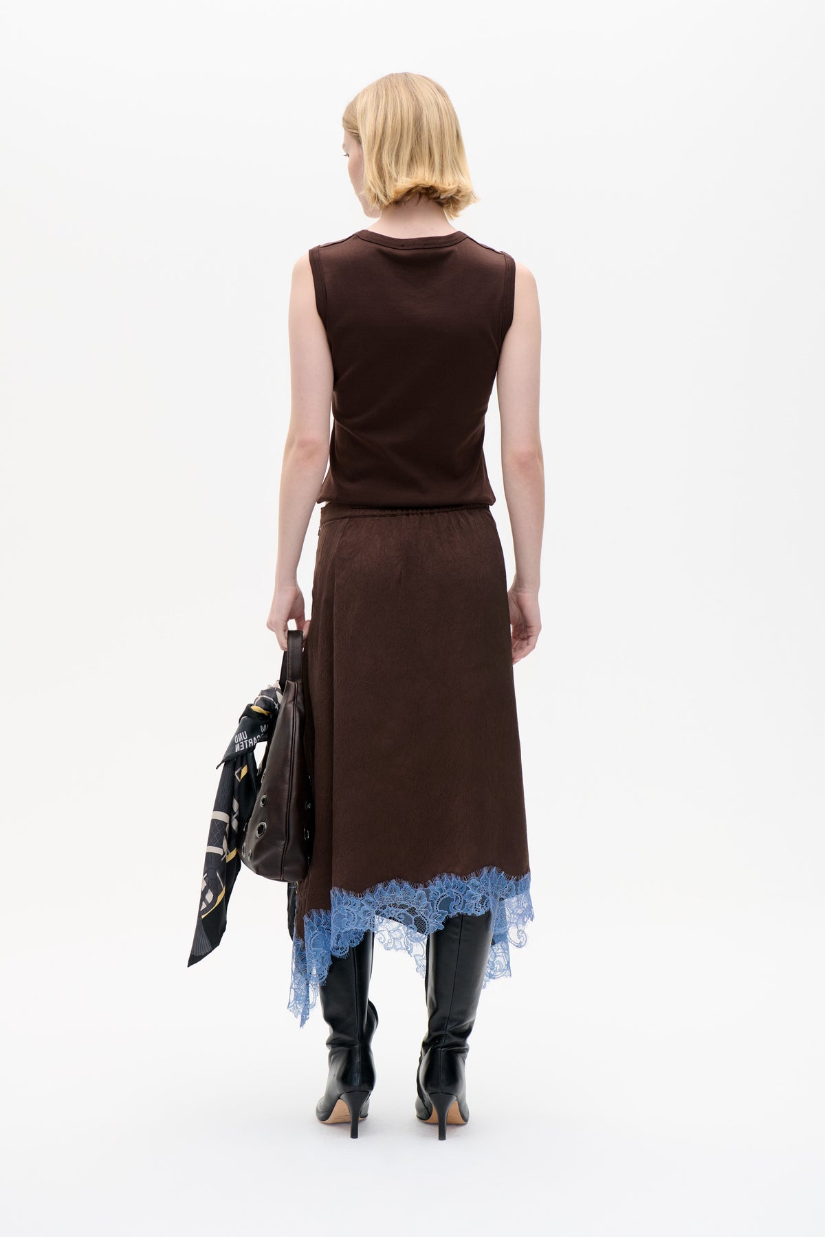 Back view of a model wearing a dark brown sleeveless top and matching skirt with blue lace trim, paired with black boots.