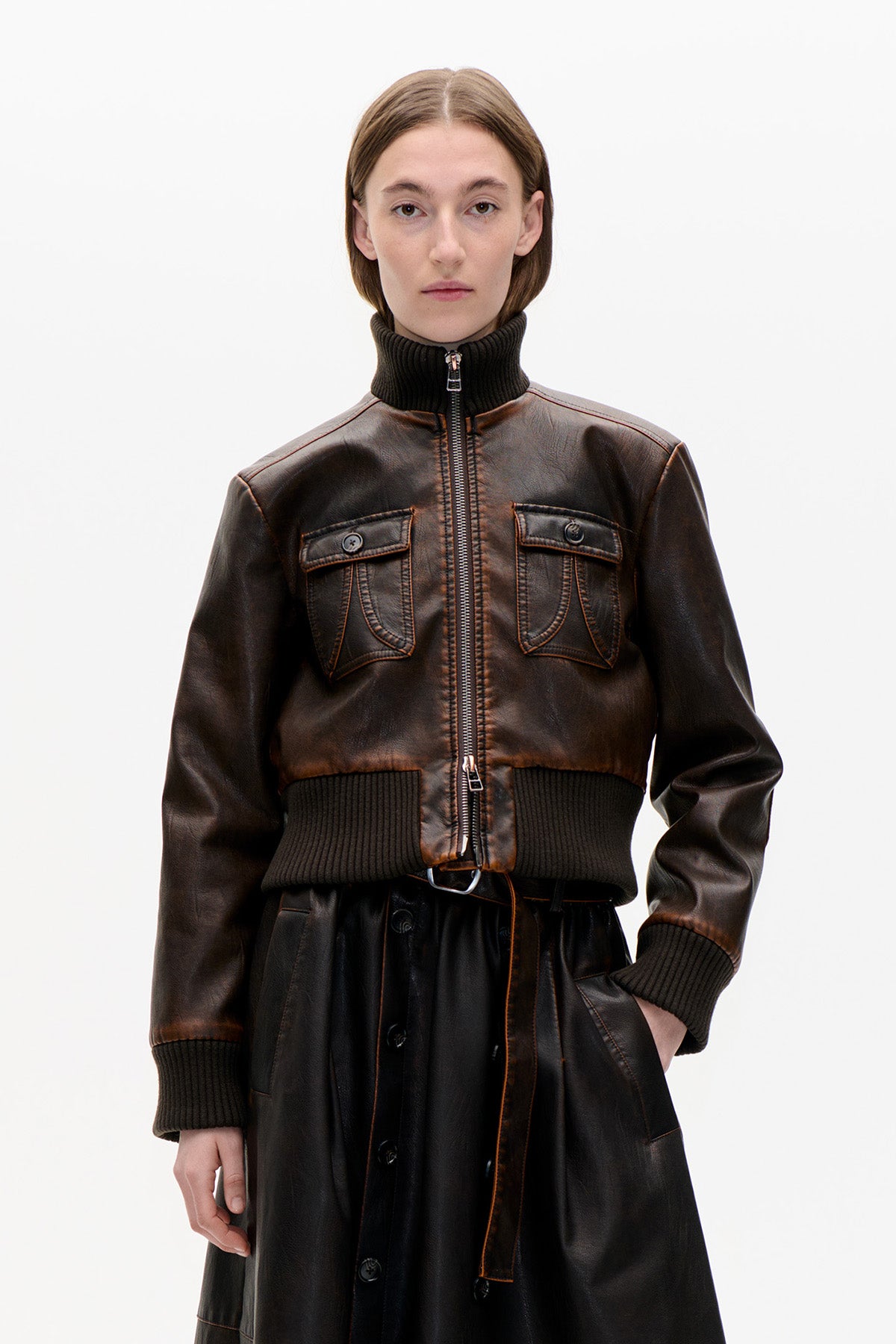 Front view of a dark brown leather-look zip jacket with a ribbed black collar, cuffs and hem, worn over a black skirt.