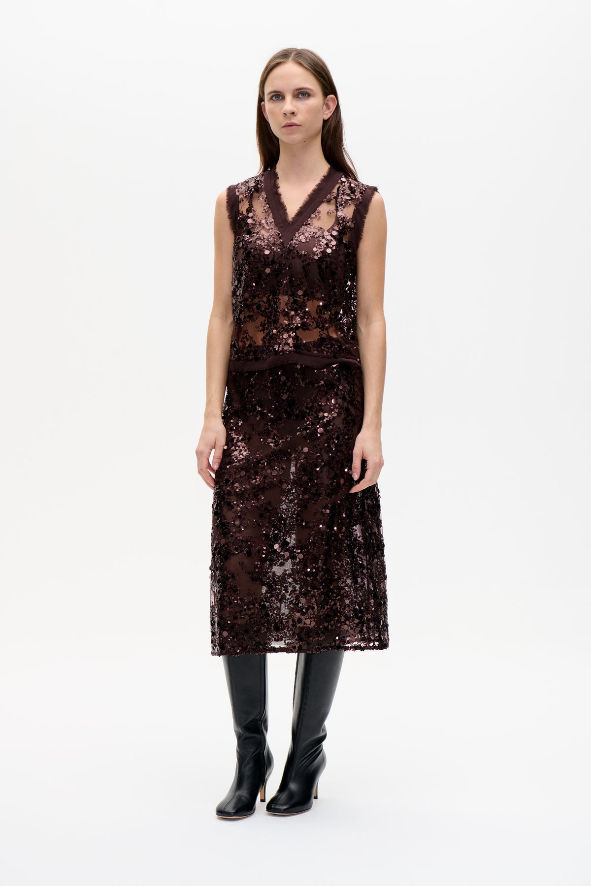 Front view of a model wearing a sleeveless dark brown V-neck dress with pink and black sequins, sheer sections and dark trim.