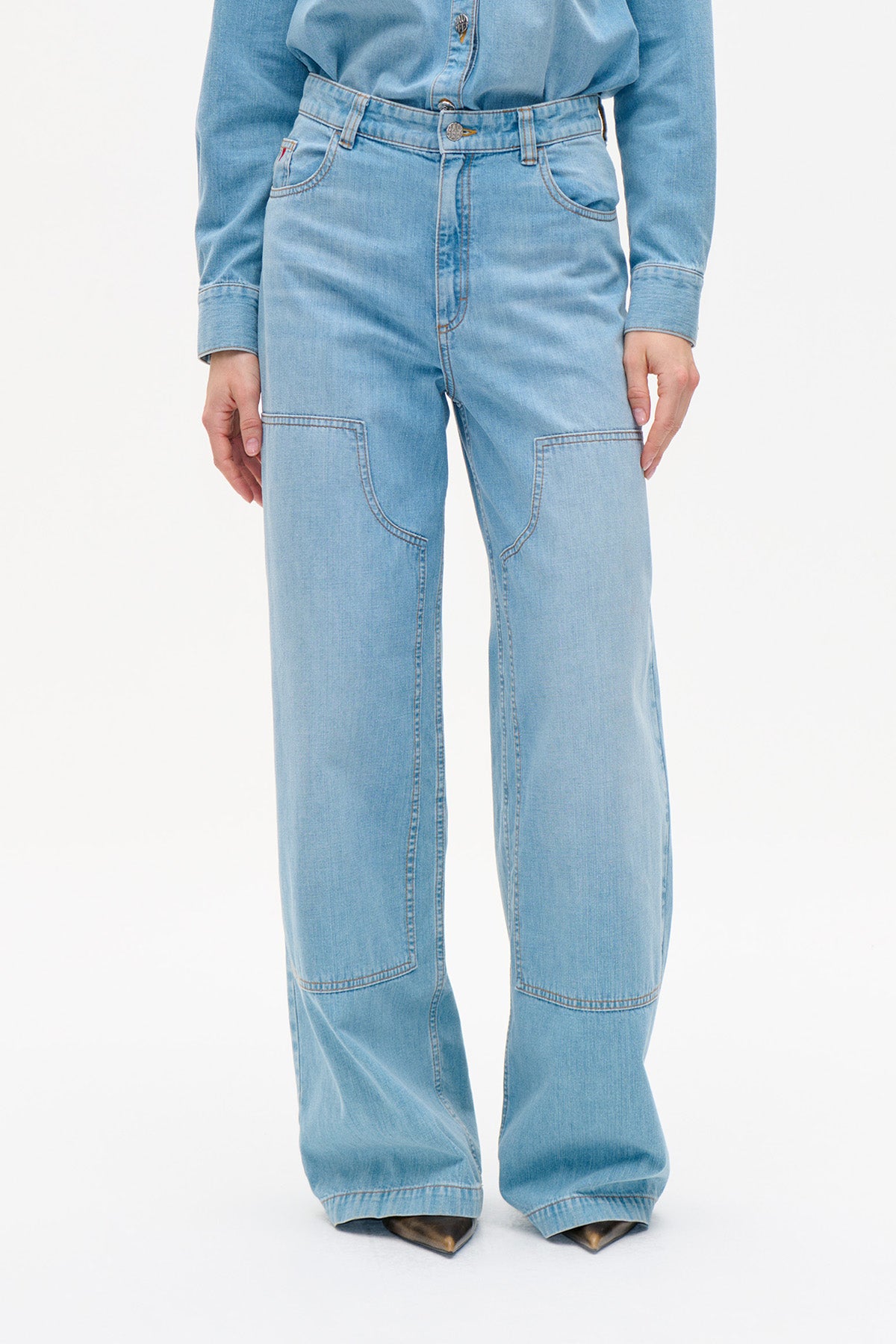 Vooraanzicht van lichtgewassen jeans met wijde pijpen en grote gebogen kniepanelen, gedragen met een blauwe denimblouse.