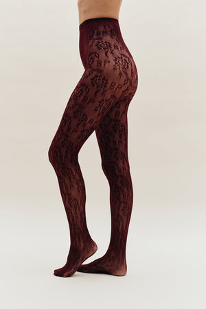 Model wearing sheer burgundy tights with an all-over dark floral pattern, shown from waist to feet.