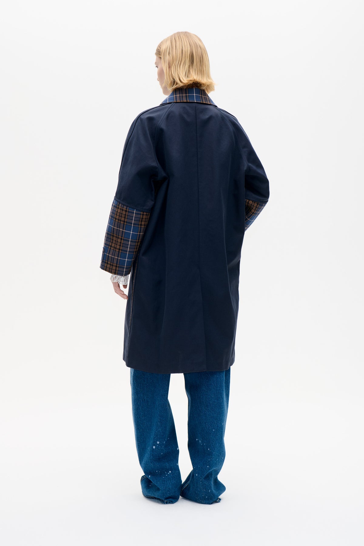 Back view of a model wearing a long navy coat with brown and blue plaid collar and turned-back cuffs.