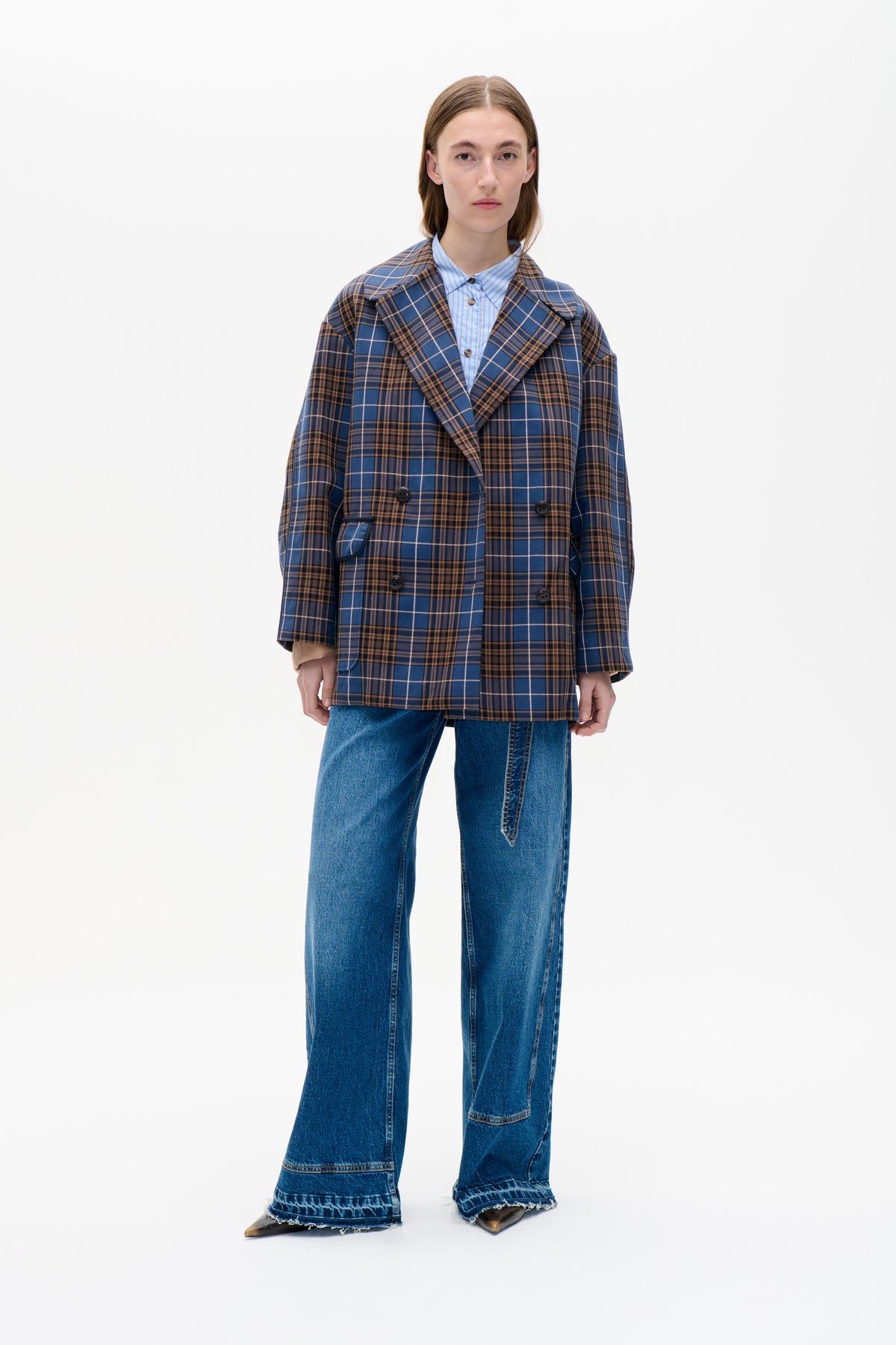 Front view of a model wearing a blue and brown plaid double-breasted coat over a light blue striped shirt and jeans.