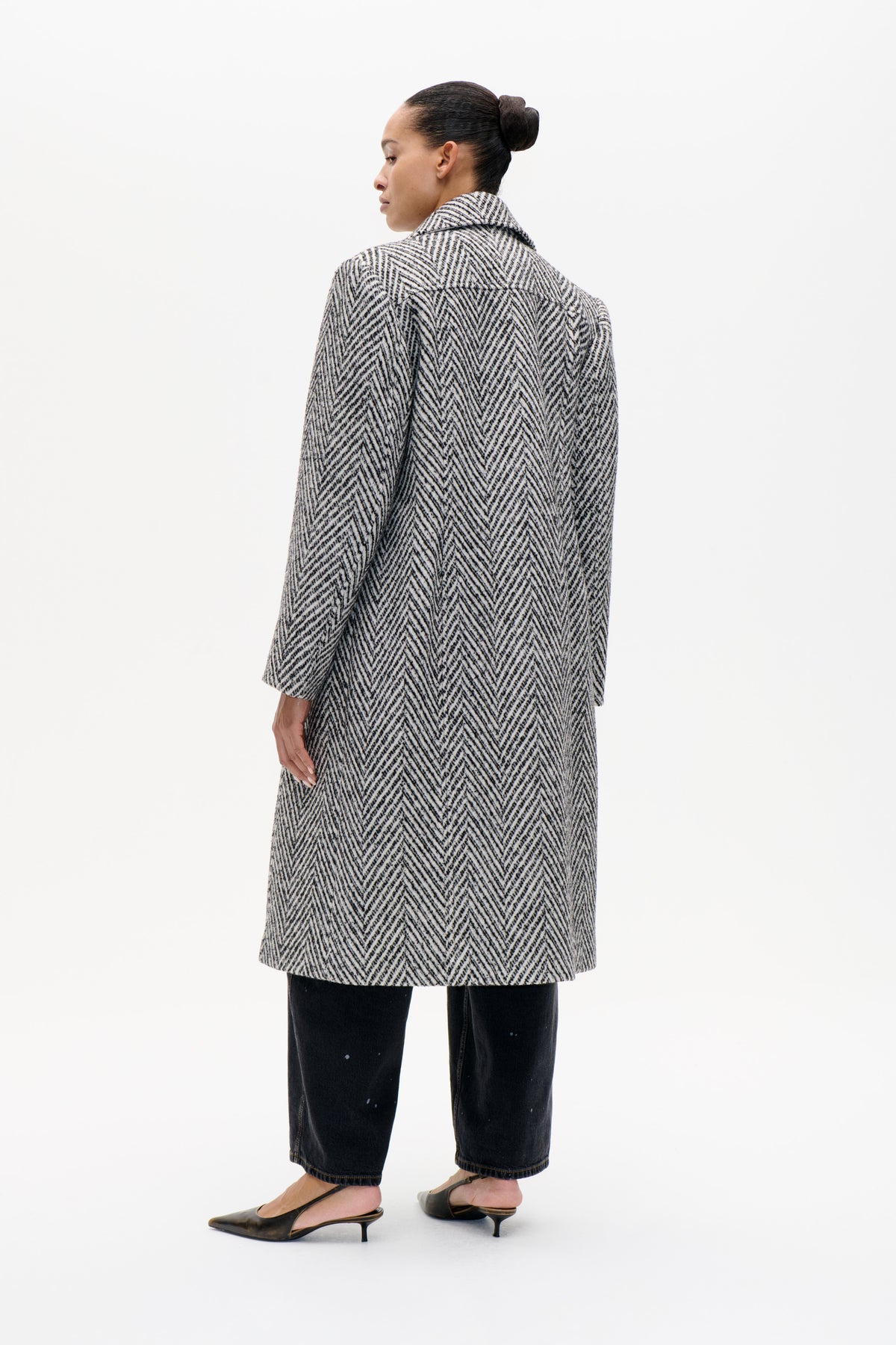 Model wearing a long black-and-cream chevron-patterned coat, shown from the side and back with a wide collar.