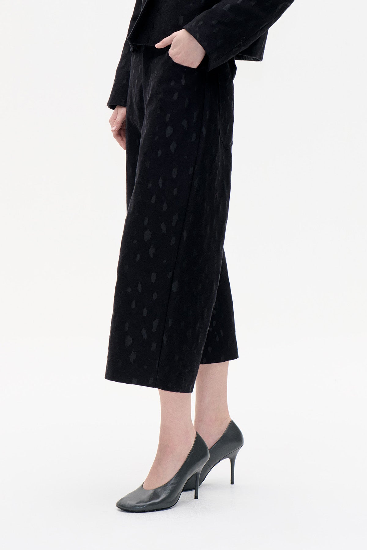 Cropped view of black wide-leg cropped trousers with a subtle irregular tonal pattern and side pockets.