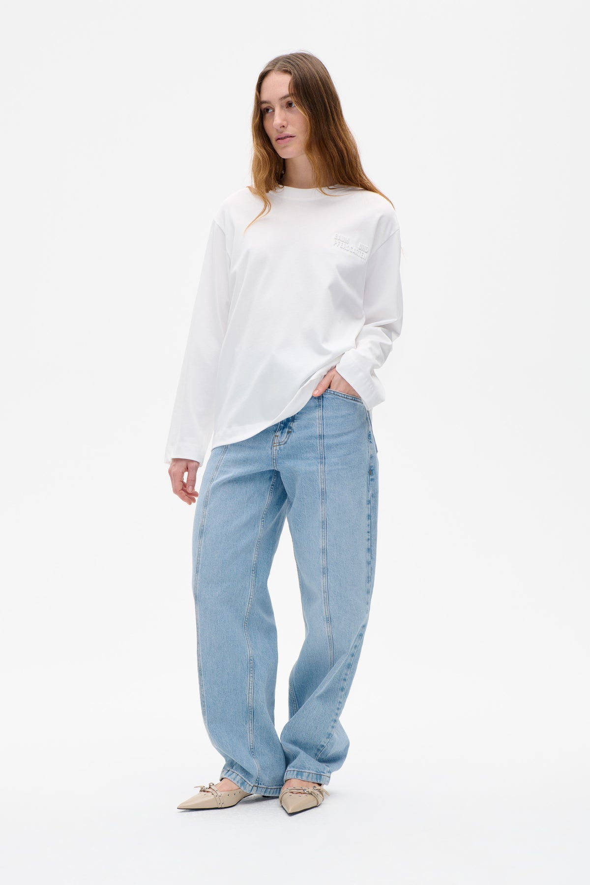 Model wearing a white long-sleeved sweatshirt with tonal raised Baum und Pferdgarten lettering on the chest, styled with light blue jeans.