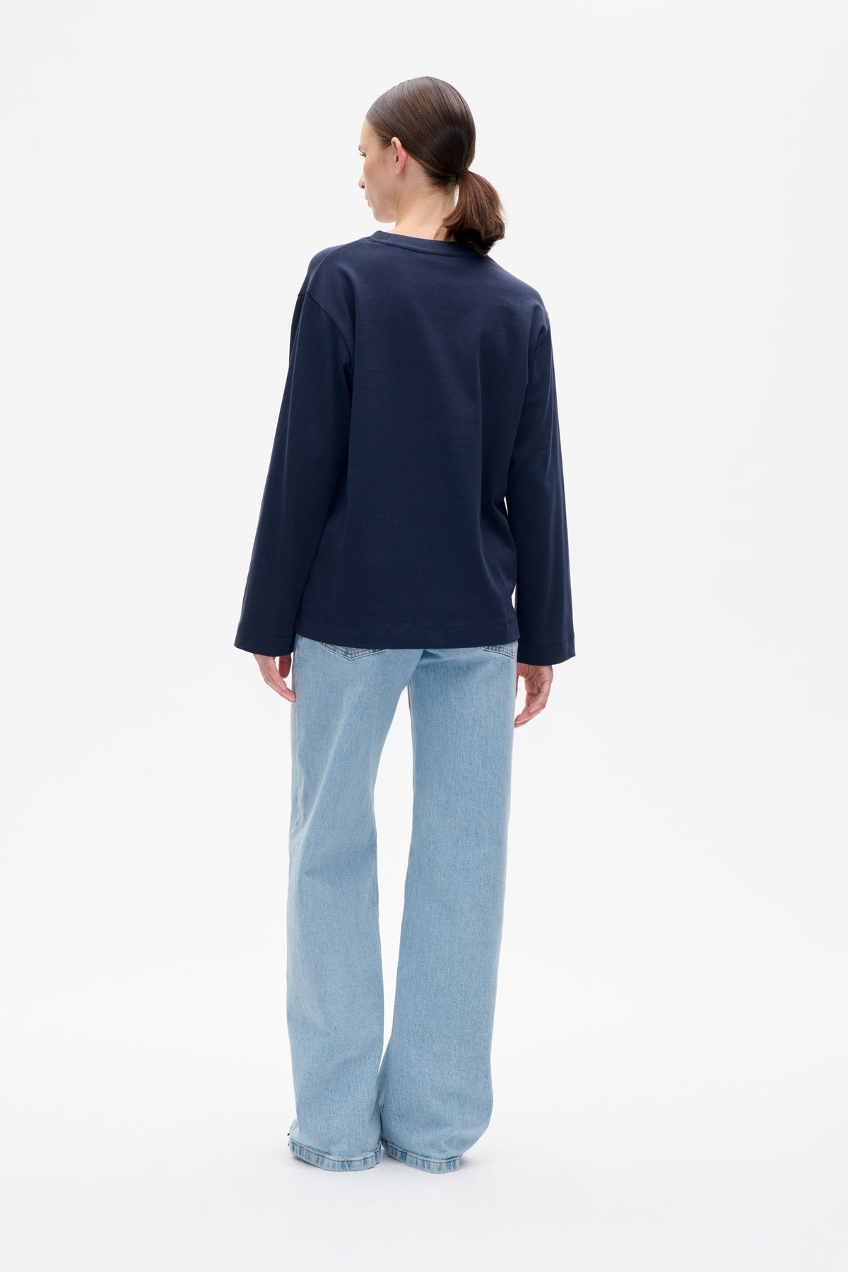 Vue de dos d’un mannequin portant un sweat-shirt uni bleu marine à manches longues et un jean bleu clair à coupe large.
