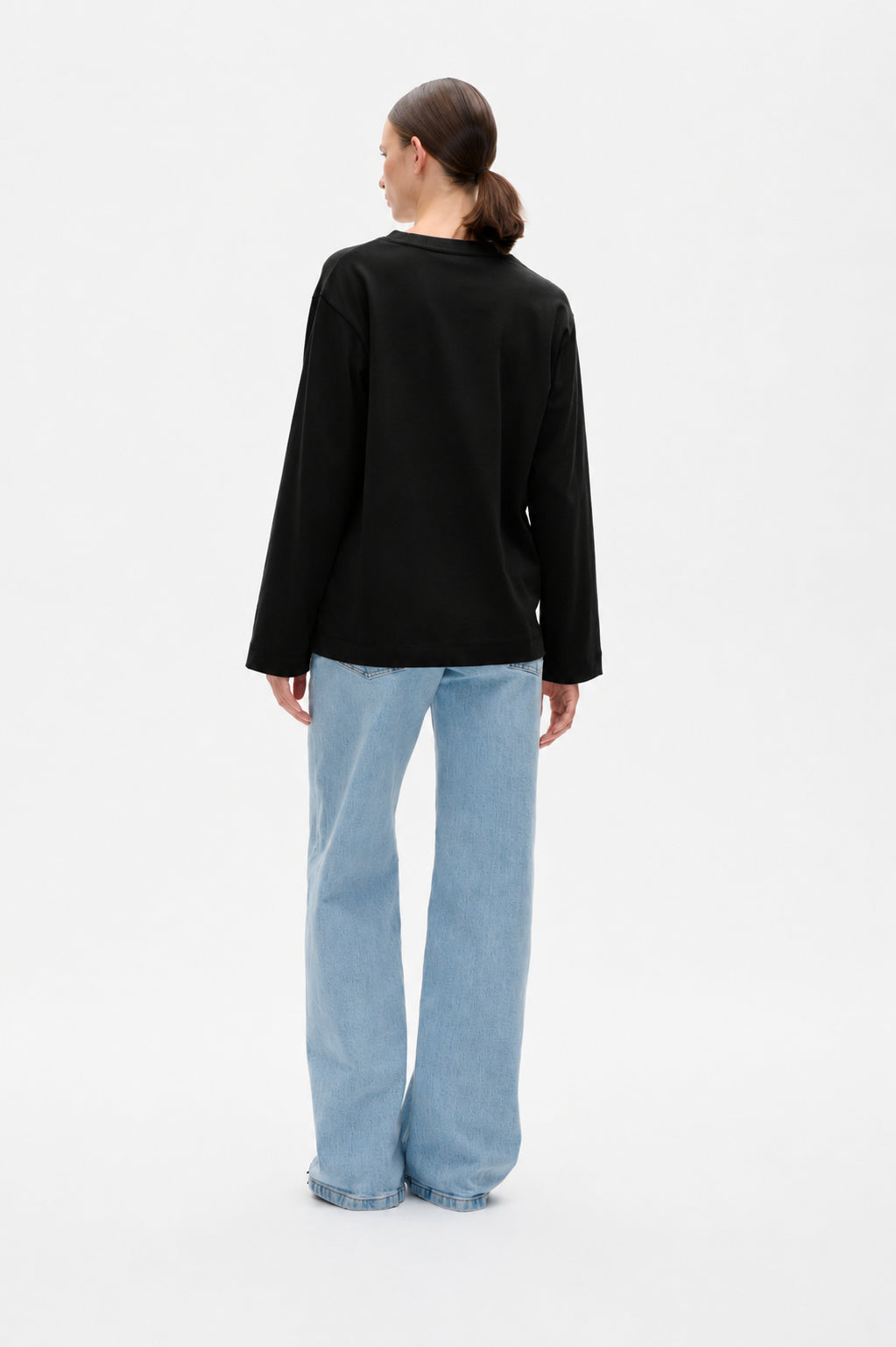 Back view of a model wearing a plain black long-sleeve top with light blue wide-leg jeans.