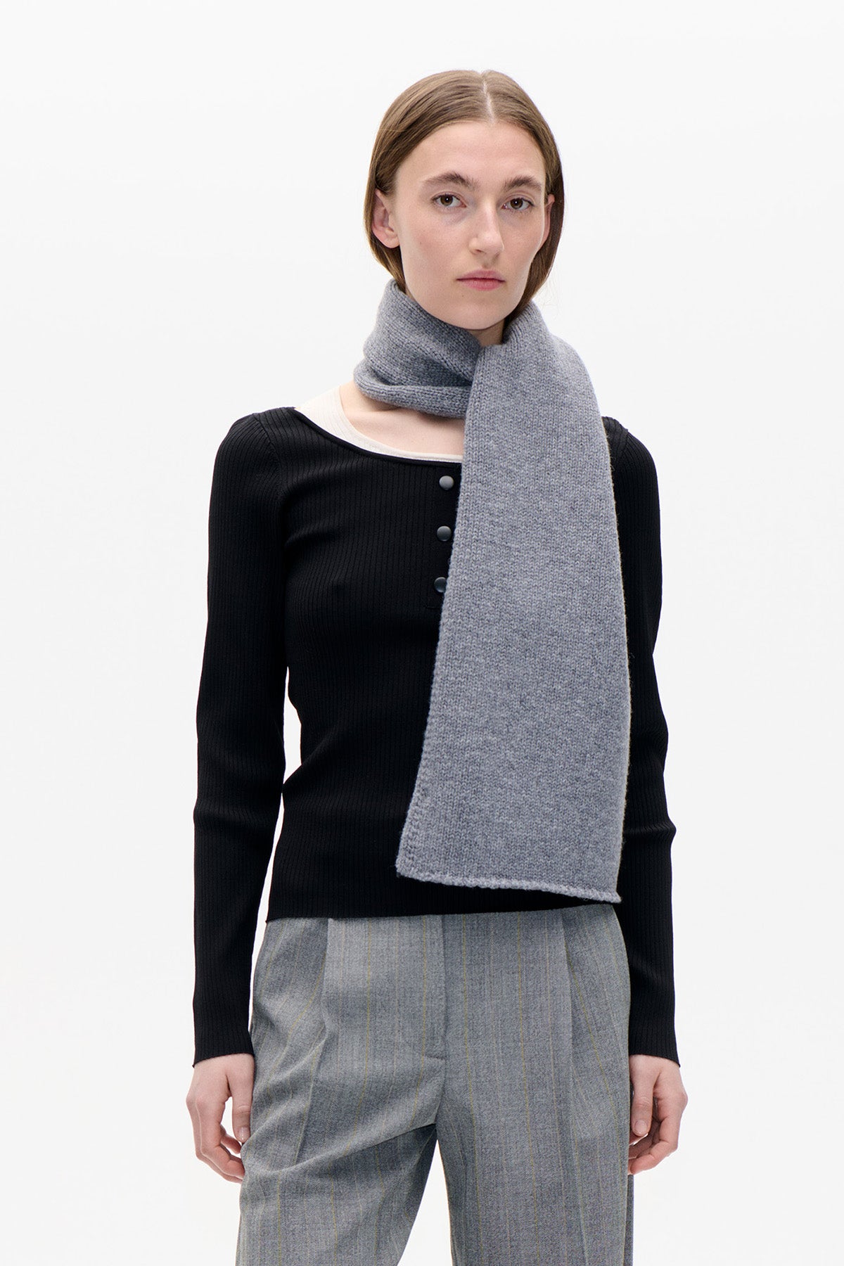 Model wearing a long heather-grey scarf over a black ribbed button-front top and grey pinstriped trousers.