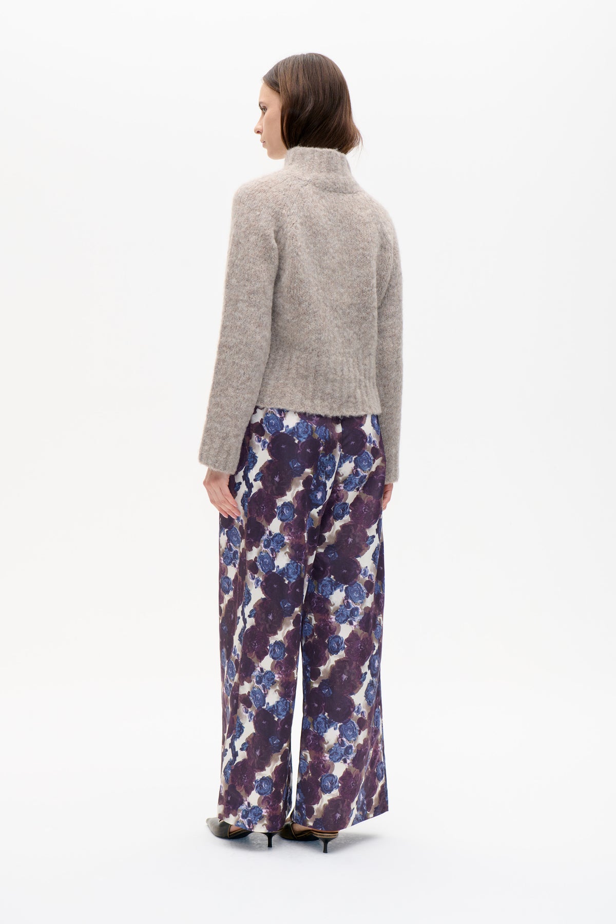 Model in profile wearing a light taupe high-neck knit sweater and wide-leg trousers with a bold blue and purple floral print.