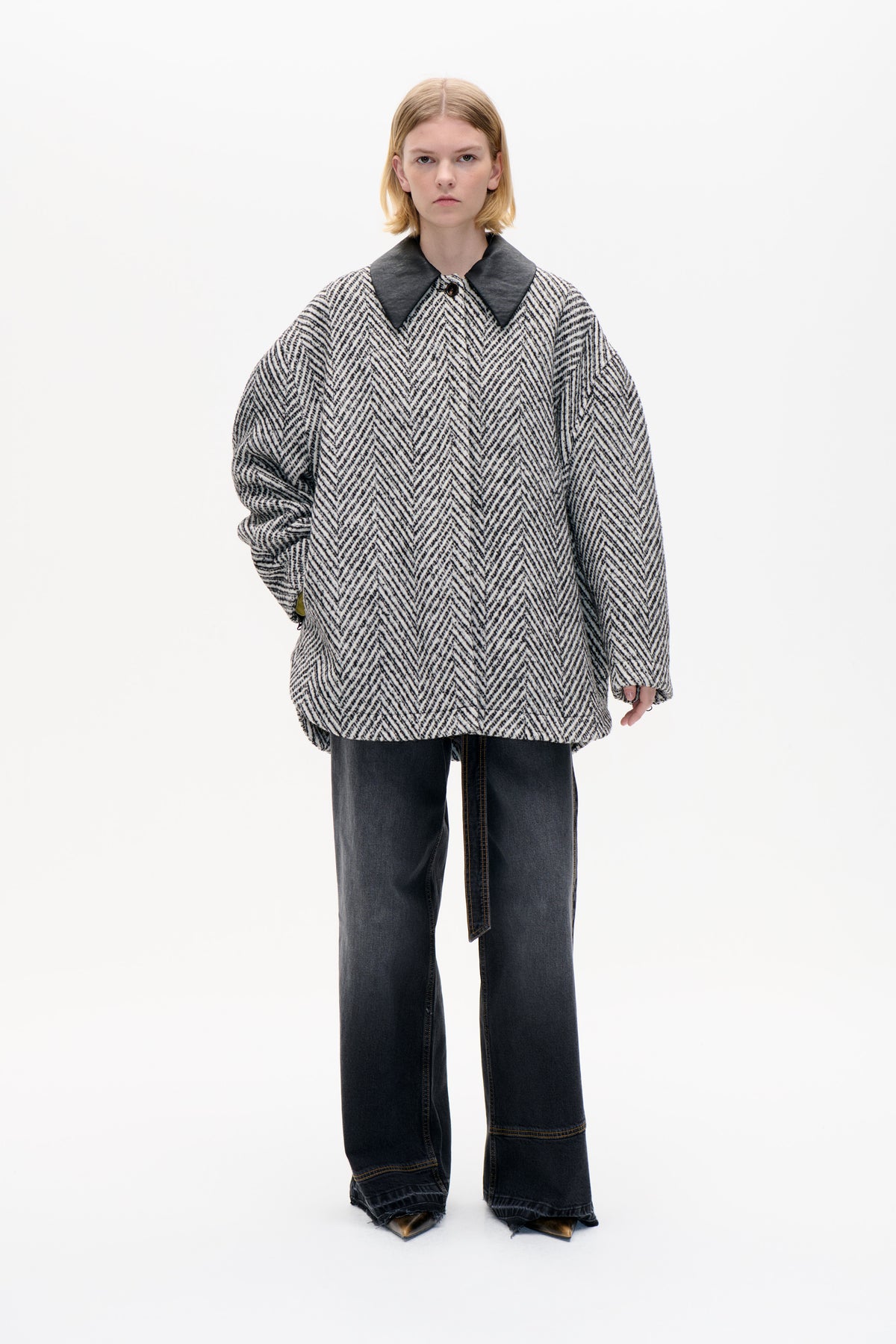 Front view of an oversized black-and-cream chevron coat with a wide charcoal collar and button, styled with dark wide-leg jeans.