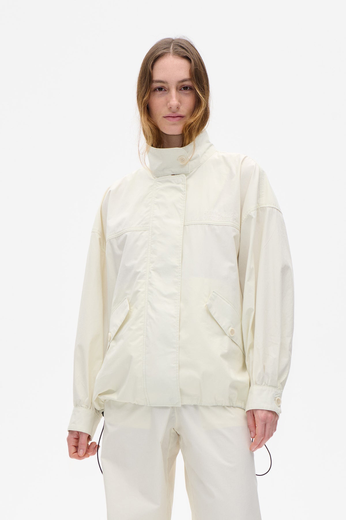 Front view of an ivory jacket with a high buttoned collar, concealed front fastening, curved chest seams and angled flap pockets.