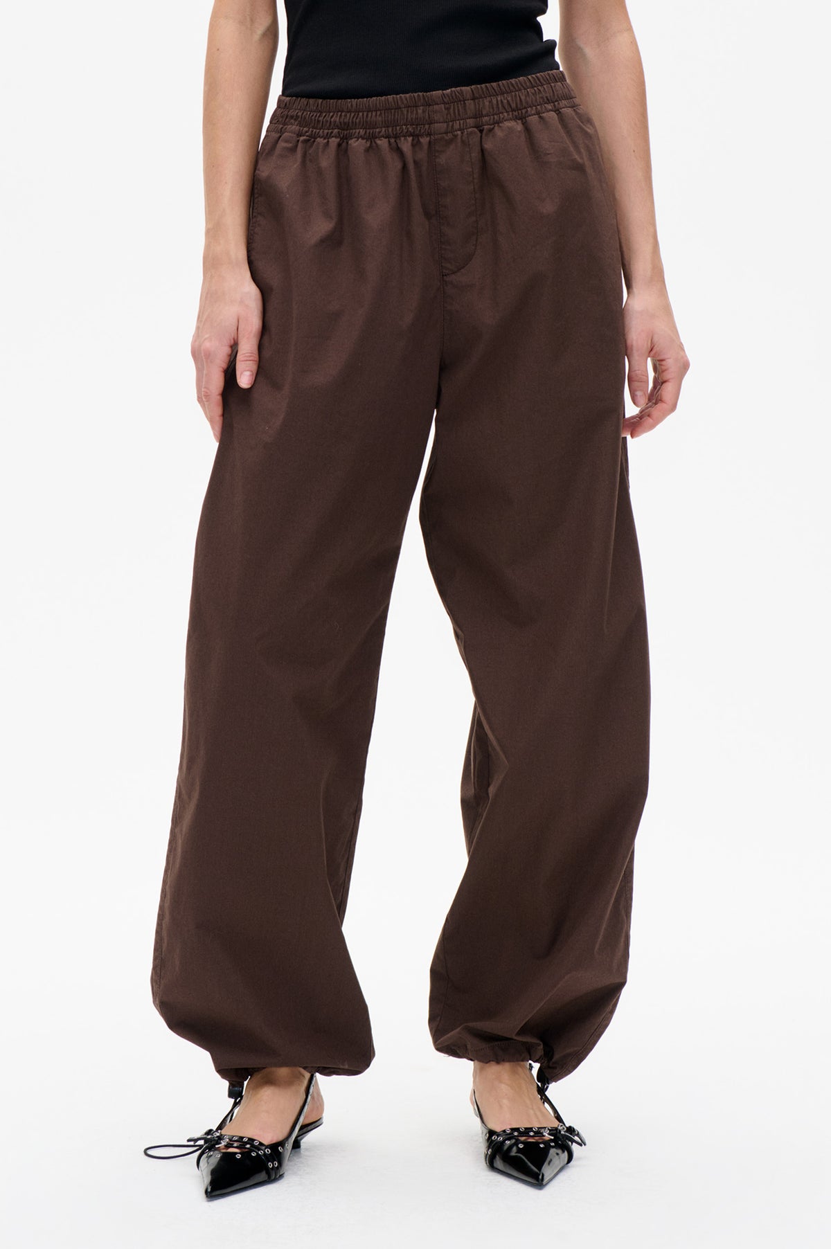 Front detail of dark brown trousers with a gathered elastic waistband, curved front pockets and adjustable ankle cuffs.