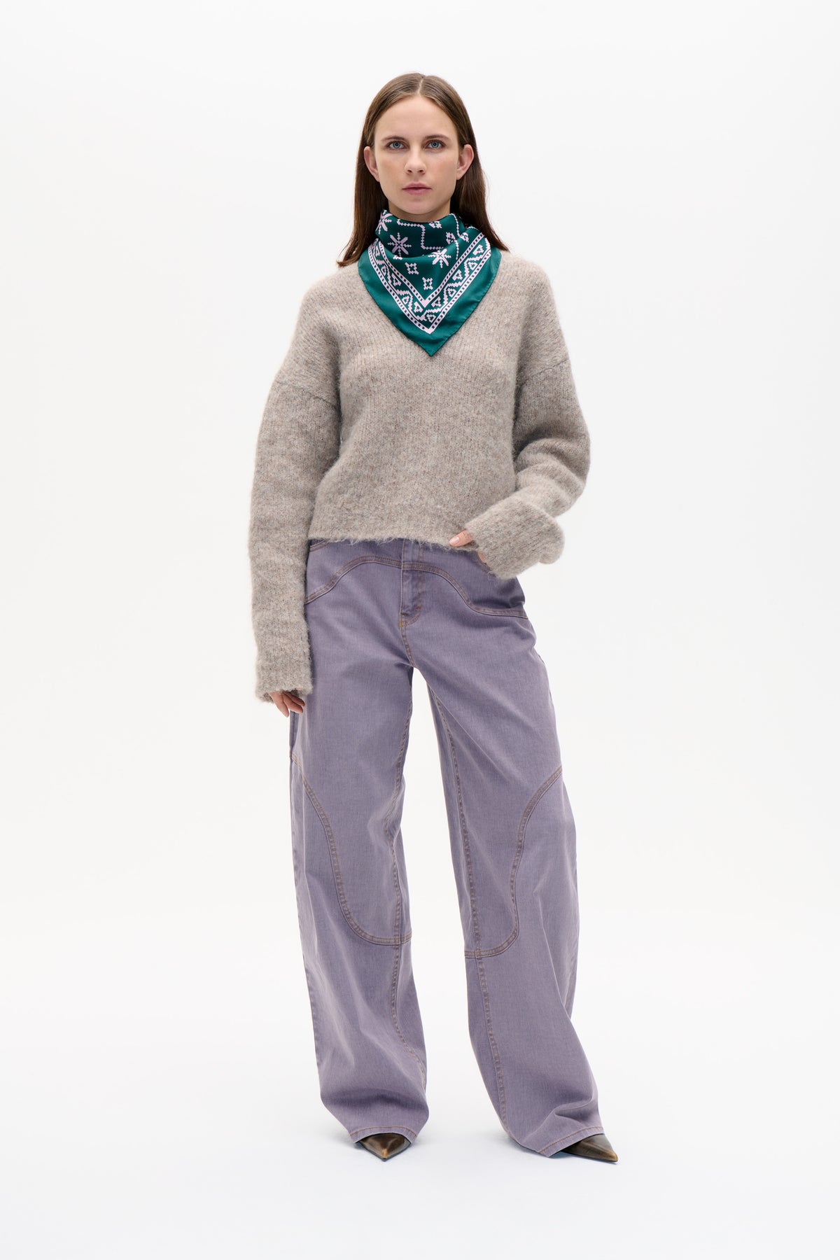 Front view of a model wearing a taupe textured sweater, teal geometric-print neck scarf and lilac wide-leg jeans.