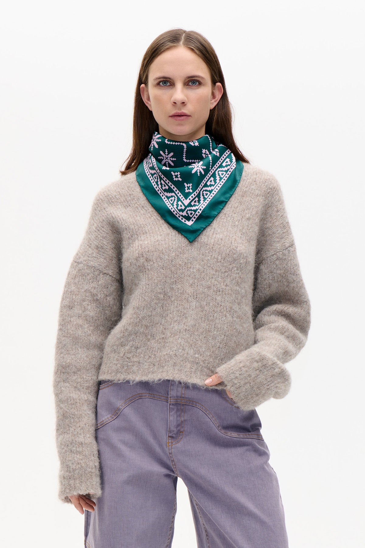 Front view of a model wearing a loose beige-grey knit sweater, teal geometric-print neck scarf and lavender wide-leg trousers.