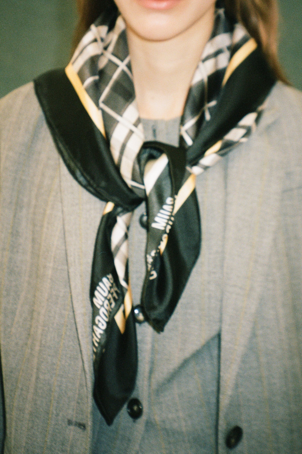Grainy close-up of a model wearing a black garment with cream geometric patterns and yellow accents over a gray top