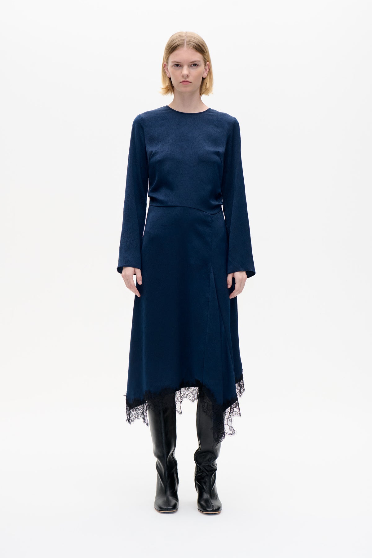 Front view of a model wearing a navy long-sleeved dress with a crinkled texture and black lace-trimmed hem.