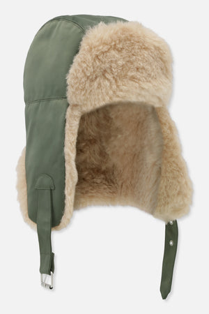 Cream fluffy trapper hat with olive green panels, long fastening straps and metal hardware, shown from the side.