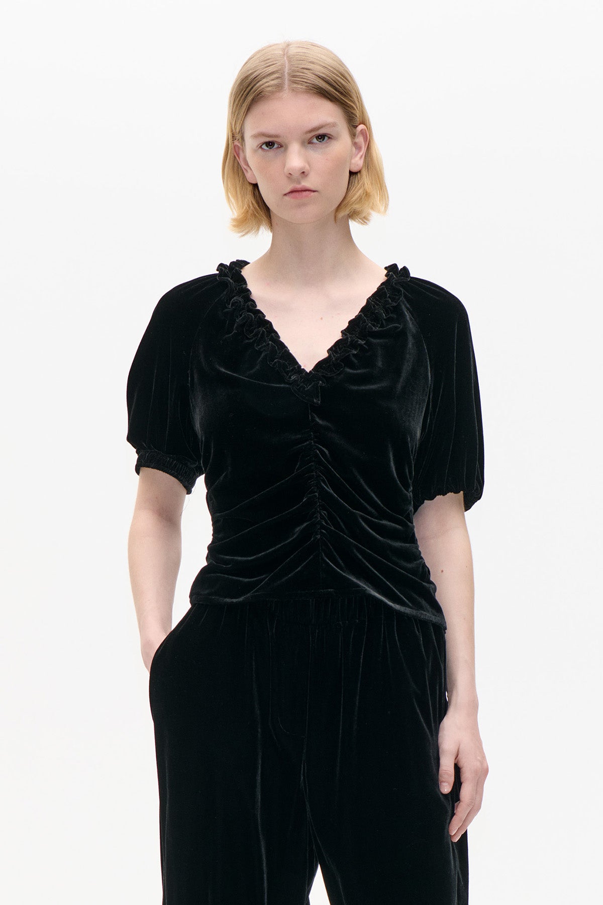Front view of a black velvet top with a ruffled V-neck, puff sleeves and gathered ruching down the front, paired with matching trousers.